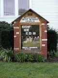 The sign indicates the correct church. It reflects some headstones from the cemetery across the street.