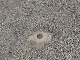 Eyelevel view of the reference mark, surrounded by rough pavement but still exposed and in good condition.